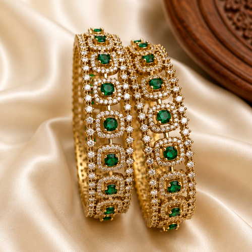Gold bangles with green gemstones on a satin surface