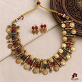 Gold necklace with red and green stones and matching earrings on a textured surface.