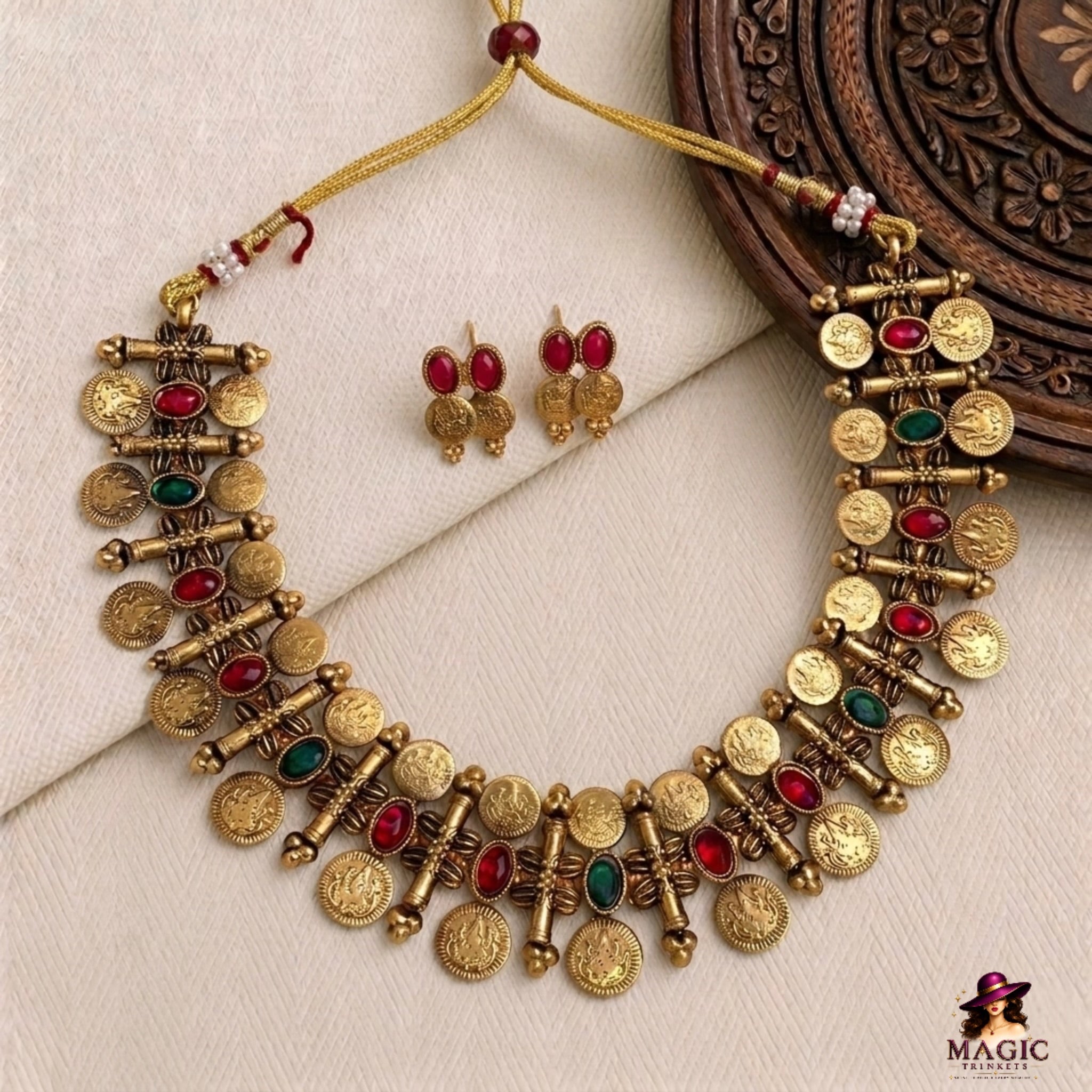 Gold necklace with red and green stones and matching earrings on a textured surface.
